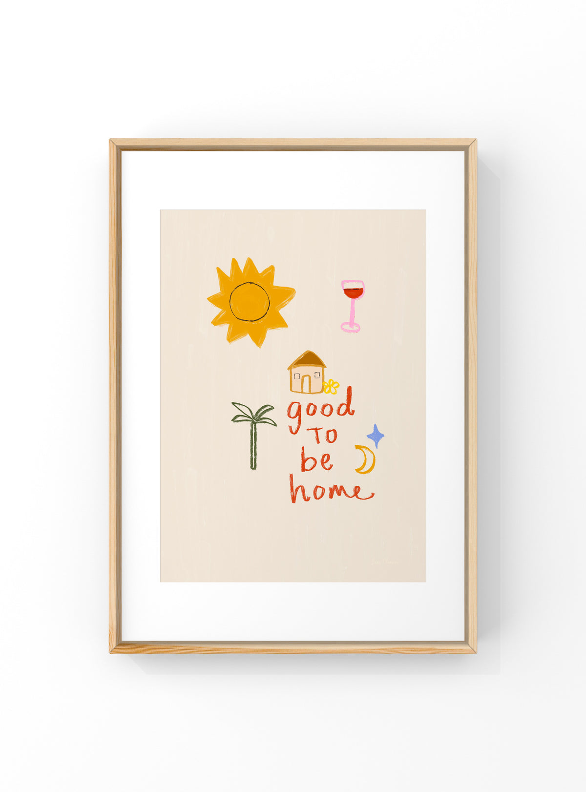 Framed wall art print with a minimalist illustration featuring a yellow sun, a pink wine glass, a small house, a palm tree, and the phrase 'good to be home' in orange and red lettering, shown in a light wood frame against a white background.